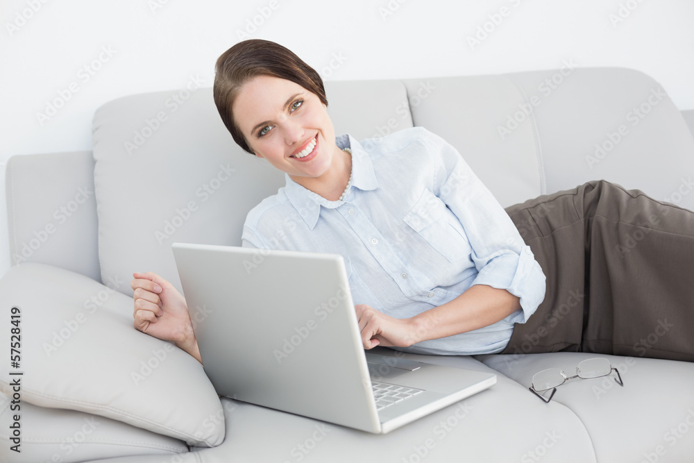 Portrait of a smiling well dressed woman using laptop on sofa Portrait of a smiling well dressed woman using laptop on sofa