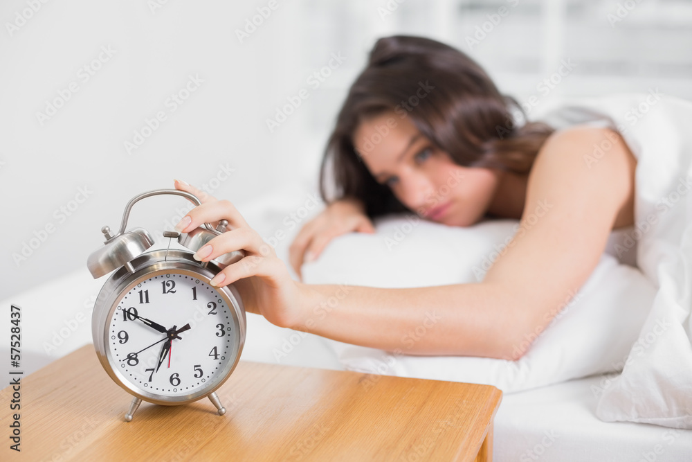 Sleepy woman in bed extending hand to alarm clock Sleepy woman in bed extending hand to alarm clock