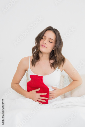 Woman with hot water bottle on stomach in bed