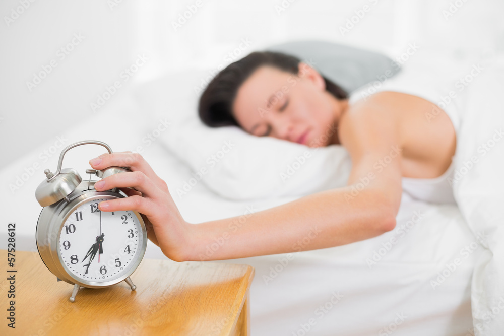 Woman in bed extending hand to alarm clock at home Woman in bed extending hand to alarm clock at home