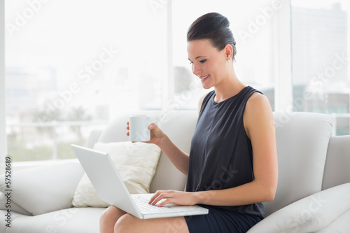 Beautiful well dressed woman using laptop while having coffee on