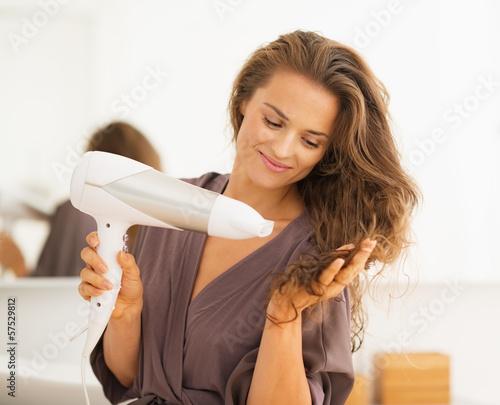 Fototapeta Happy young woman blow drying hair in bathroom