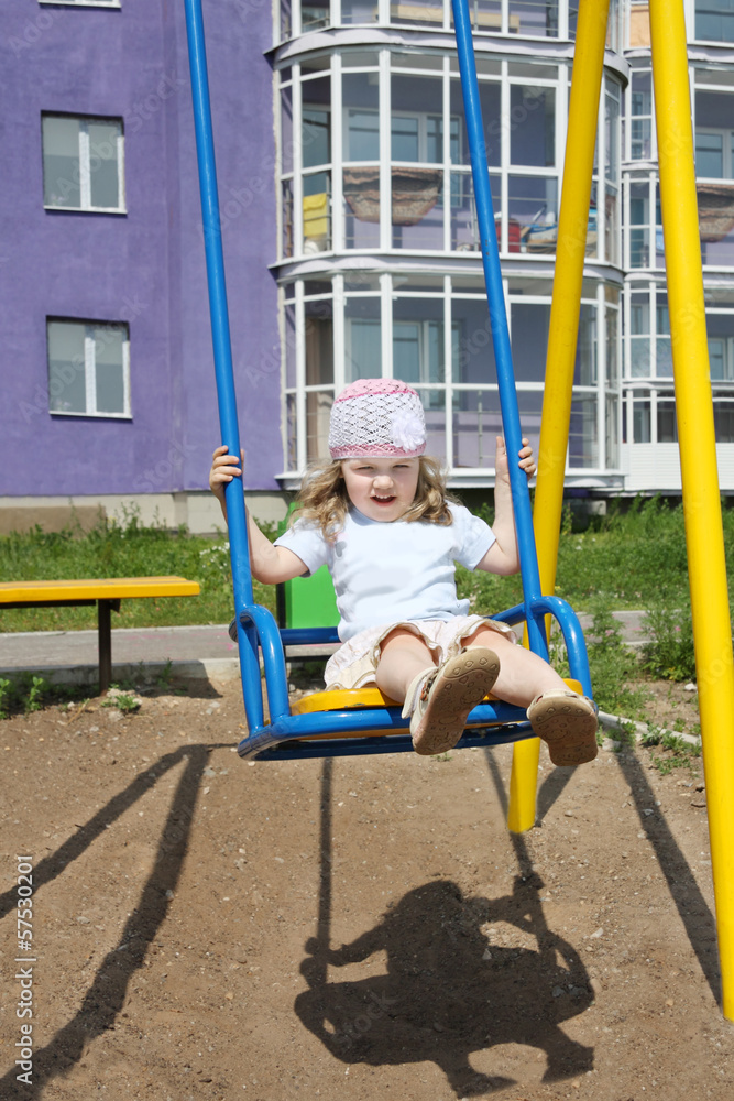 Little cute girl sits on swing at playground near building Little cute girl sits on swing at playground near building