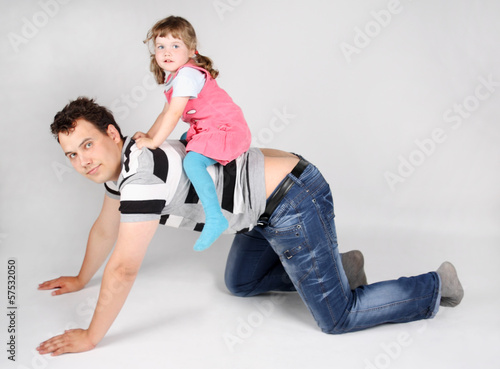 Llittle cute daughter sits on back of his father on grey backgro