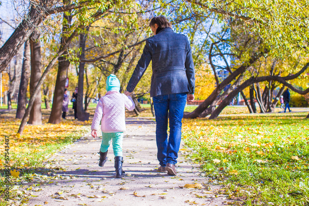 Fototapeta premium Rear view of young father and little girl walking in autumn park