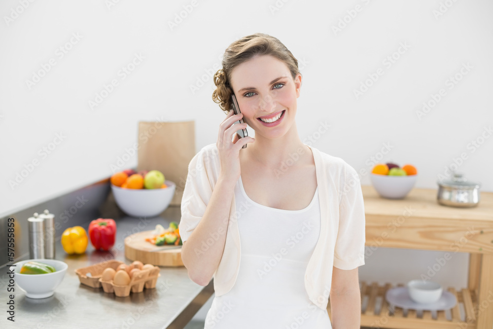 Joyful young woman phoning with her smartphone standing in kitch