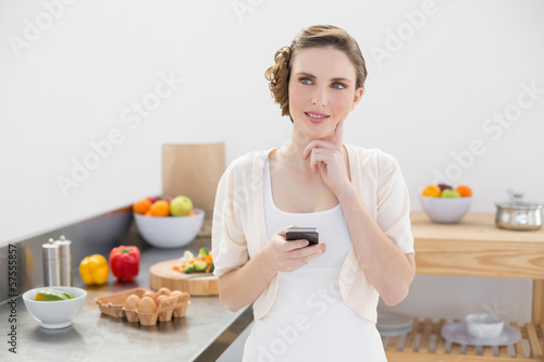 Thoughtful pretty woman holding her smartphone standing in her k