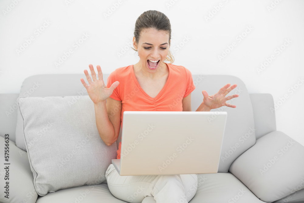 Cheering casual woman using her notebook sitting on her couch Cheering casual woman using her notebook sitting on her couch
