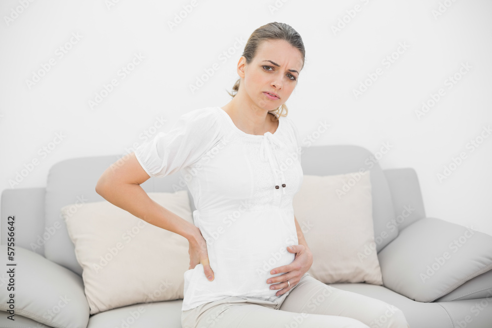 Beautiful pregnant woman looking seriously at camera holding her Beautiful pregnant woman looking seriously at camera holding her
