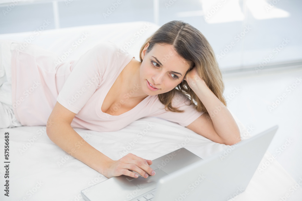 Woman using her notebook while lying on her bed Woman using her notebook while lying on her bed