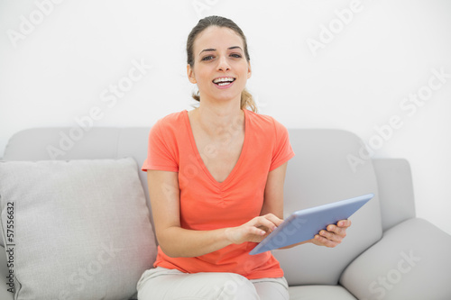 Amused casual woman using her tablet smiling cheerfully at camer