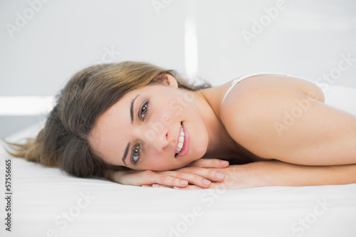 Content brunette woman smiling at camera lying on her bed