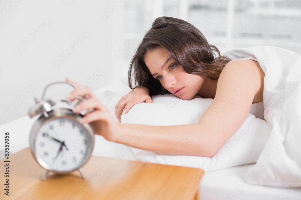 Woman in bed extending hand to alarm clock Woman in bed extending hand to alarm clock