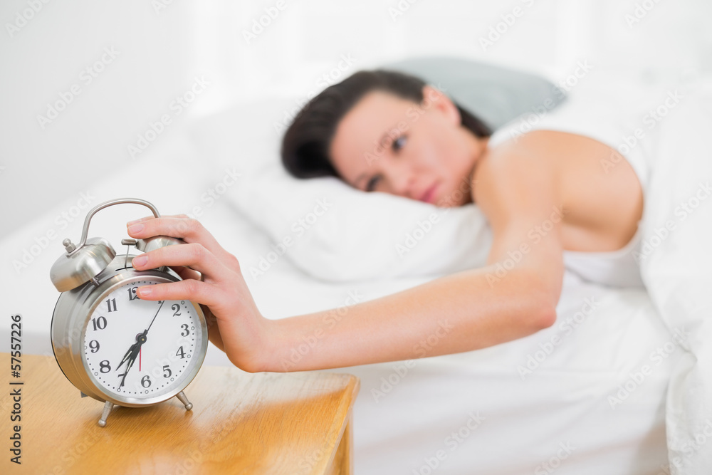 Woman in bed extending hand to alarm clock Woman in bed extending hand to alarm clock