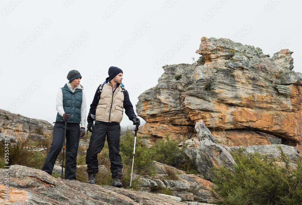 Couple on rocky landscape with trekking poles against sky