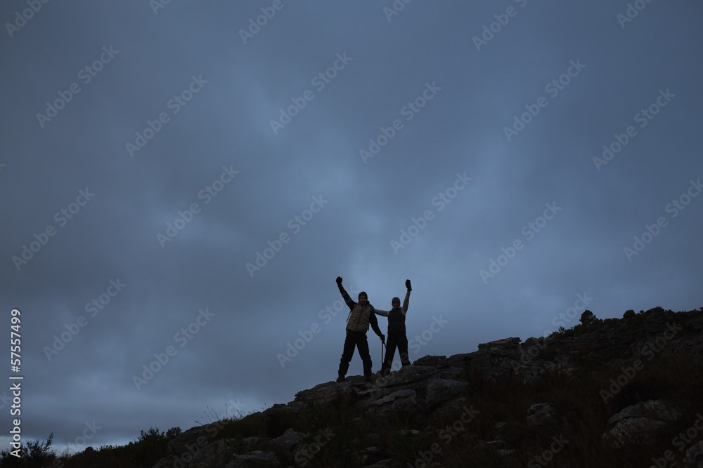 Couple raising hands on rocky landscape against sky at night