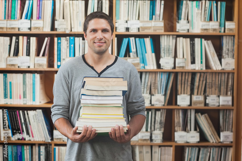 Attractive librarian holding a pile of books standing in library