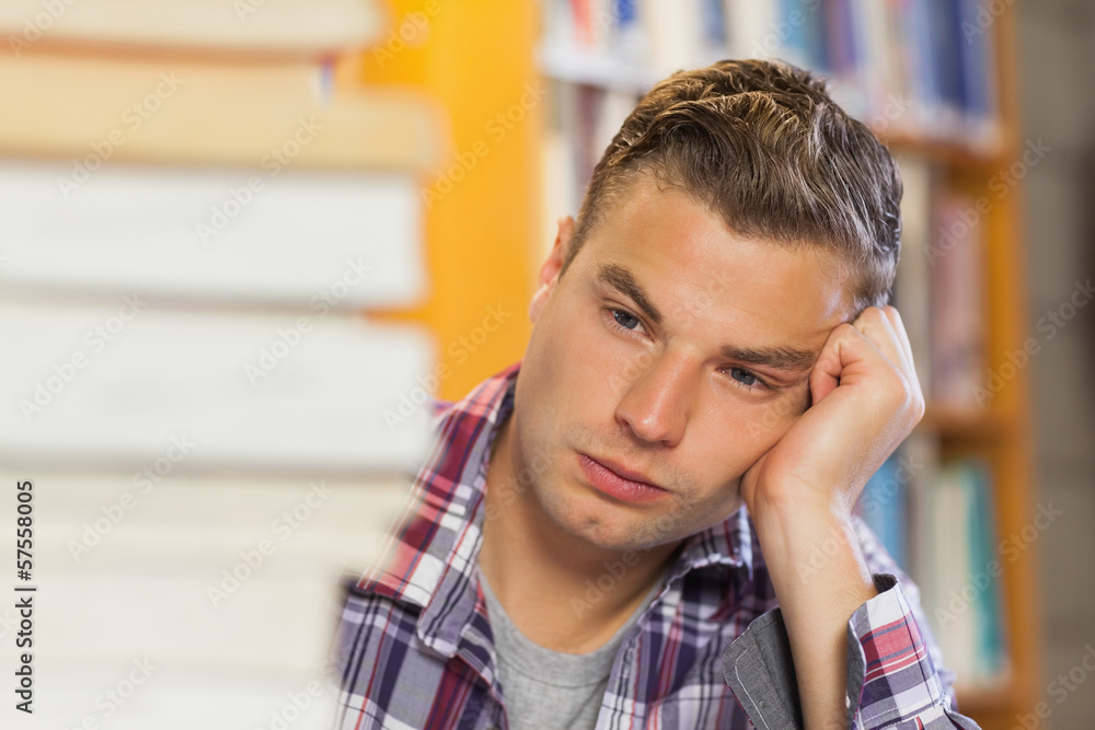Exhausted handsome student studying between piles of books Exhausted handsome student studying between piles of books