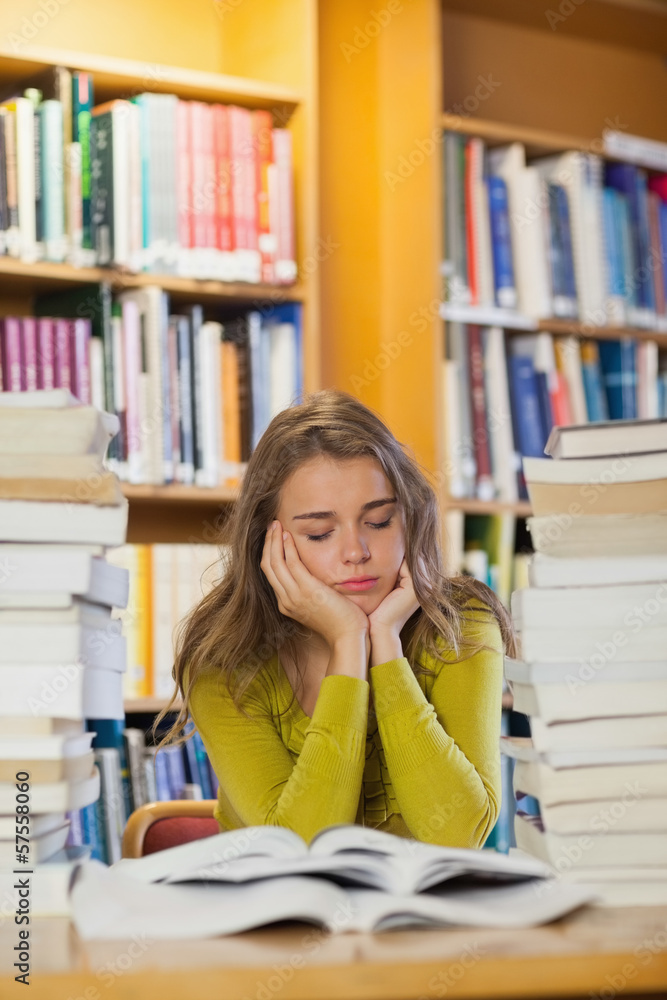 Tired beautiful student studying between piles of books with clo Tired beautiful student studying between piles of books with clo