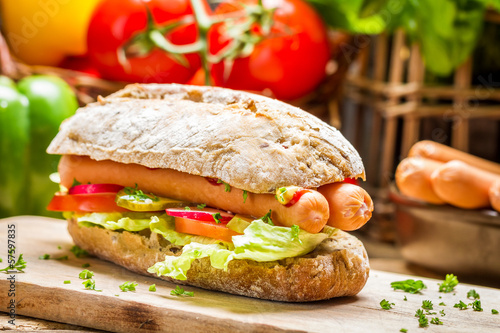 Closeup of hot dog with two sausages and fresh vegetables