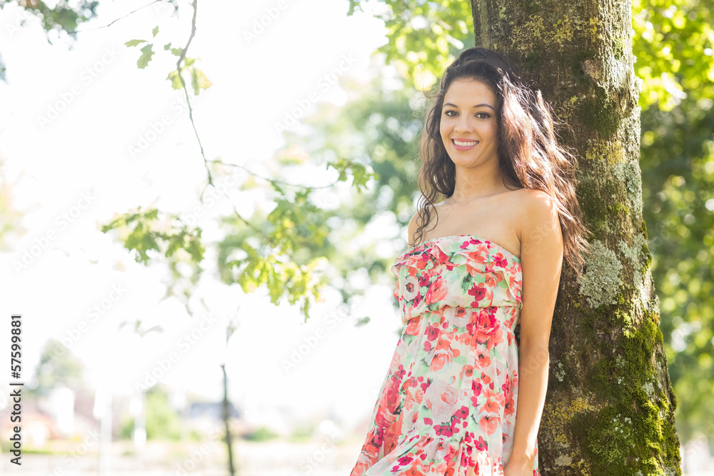Stylish smiling brunette leaning against tree