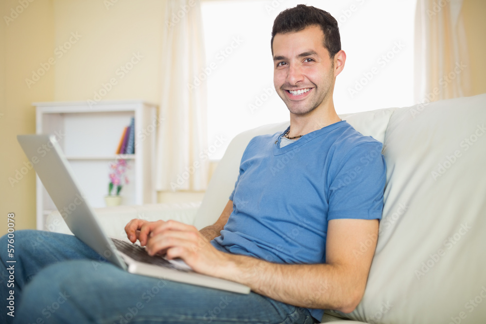 Casual content man sitting on couch using laptop looking at came