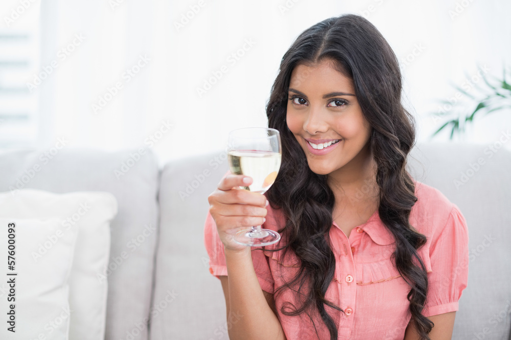 Smiling cute brunette sitting on couch holding white wine glass Smiling cute brunette sitting on couch holding white wine glass