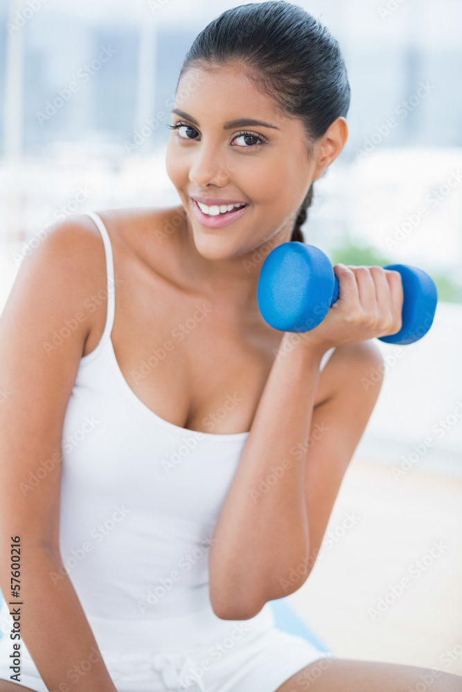 Cheerful toned brunette sitting on floor with dumbbells Cheerful toned brunette sitting on floor with dumbbells