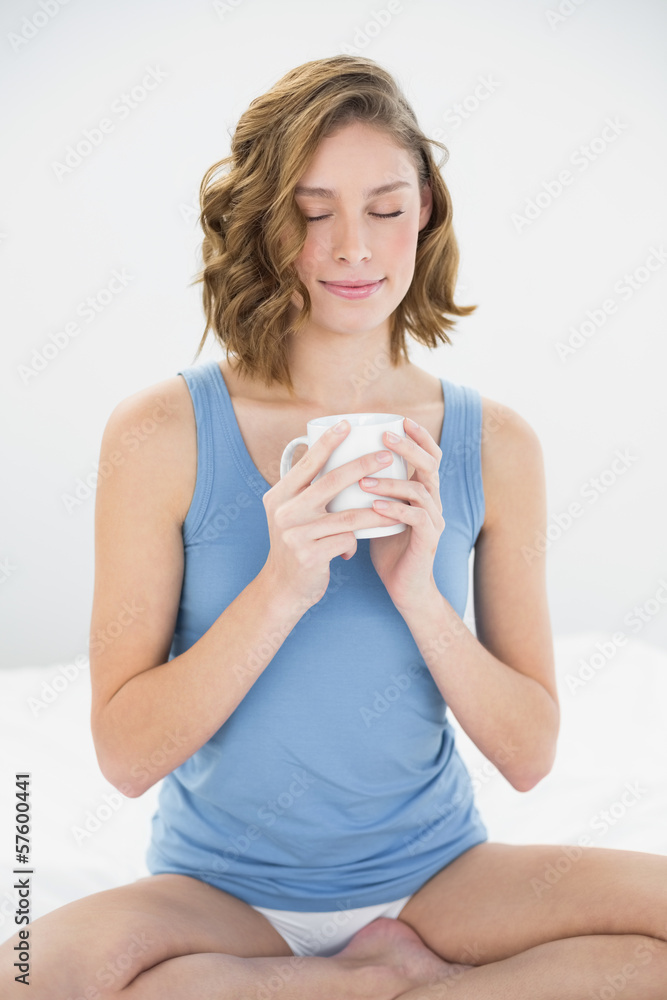 Content peaceful woman sitting on her bed holding white cup