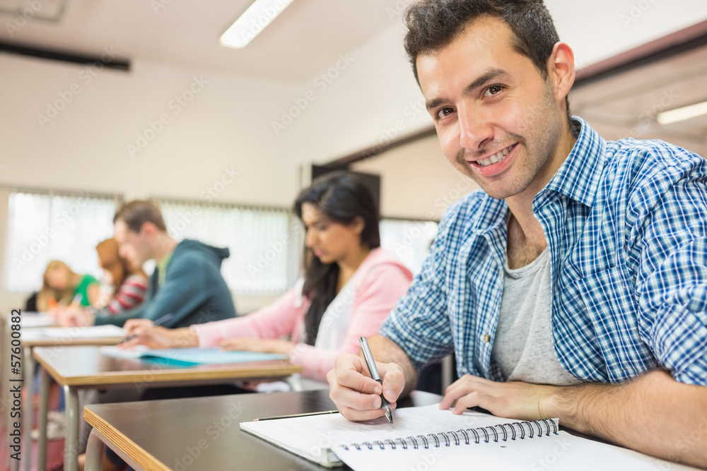 Smiling male student with others writing notes in classroom Smiling male student with others writing notes in classroom