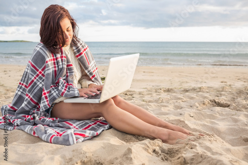 Woman covered with blanket using laptop at beach