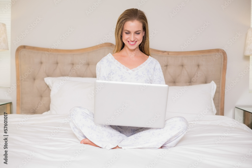 Natural smiling woman sitting on bed using laptop Natural smiling woman sitting on bed using laptop