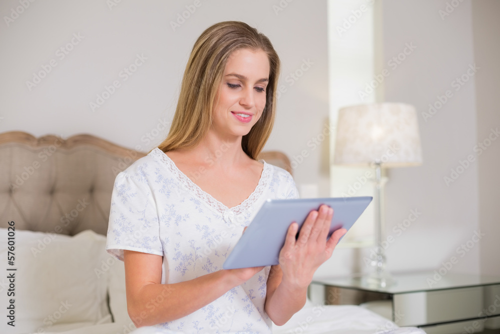 Natural happy woman sitting on bed holding tablet