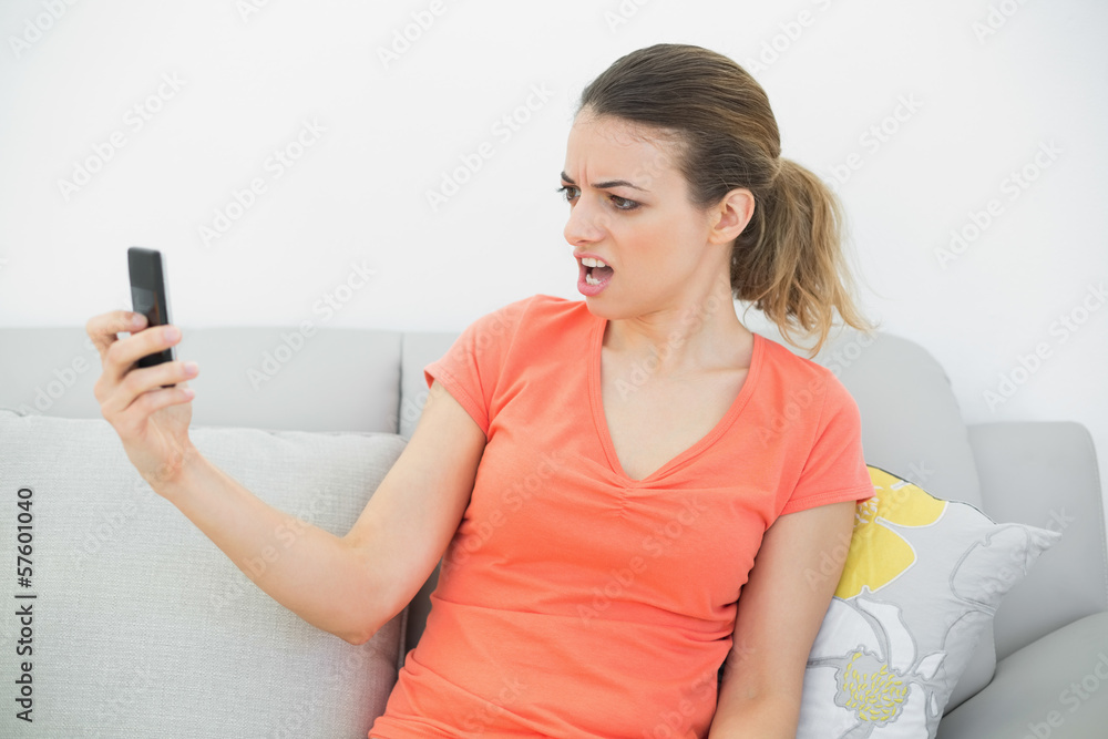Shocked woman looking at her smartphone sitting on couch Shocked woman looking at her smartphone sitting on couch
