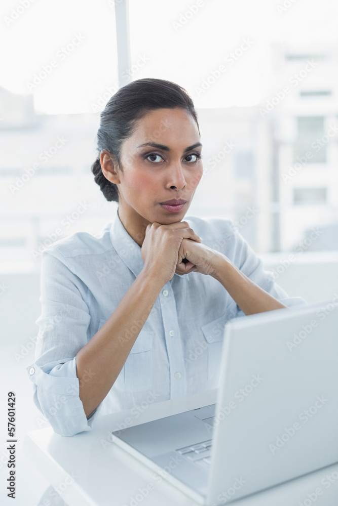 Serious dark haired woman looking at camera sitting at her desk Serious dark haired woman looking at camera sitting at her desk