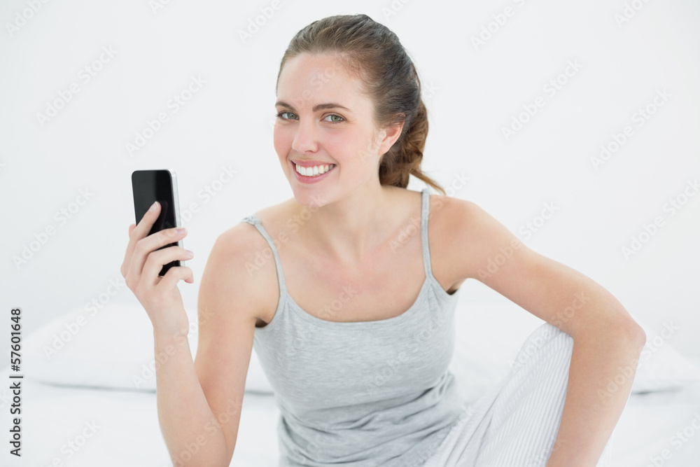 Smiling woman with mobile phone sitting in bed Smiling woman with mobile phone sitting in bed