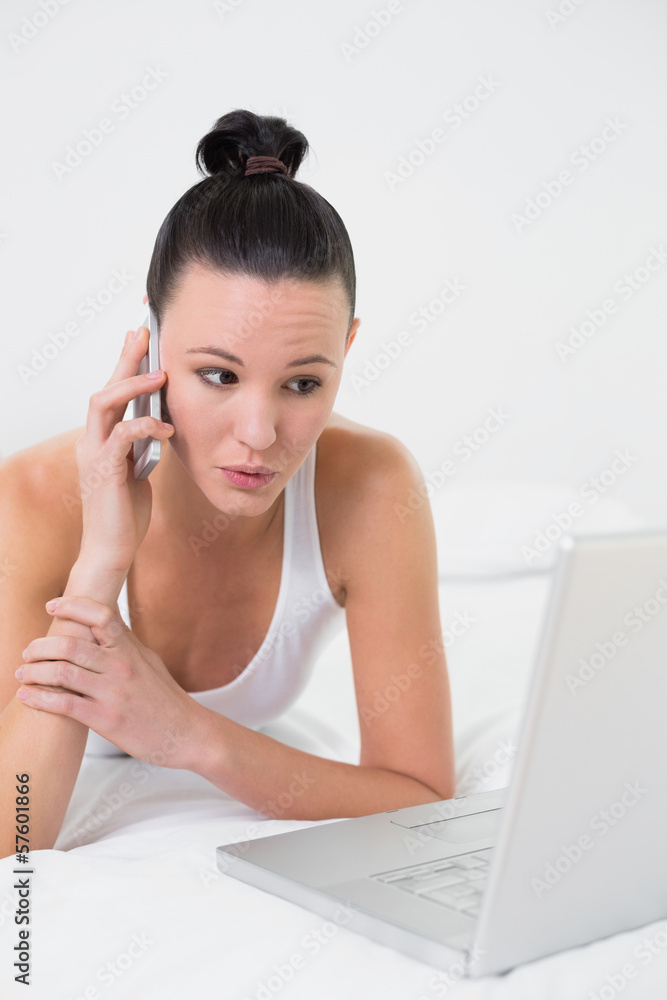 Shocked casual woman using cellphone and laptop in bed Shocked casual woman using cellphone and laptop in bed