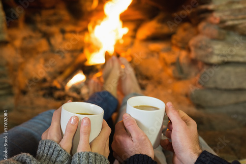 Bild auf Leinwand Hands holding coffee cups in front of lit fireplace