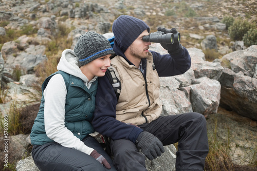 Couple sitting on rock with binoculars while on a hike © lightwavemedia