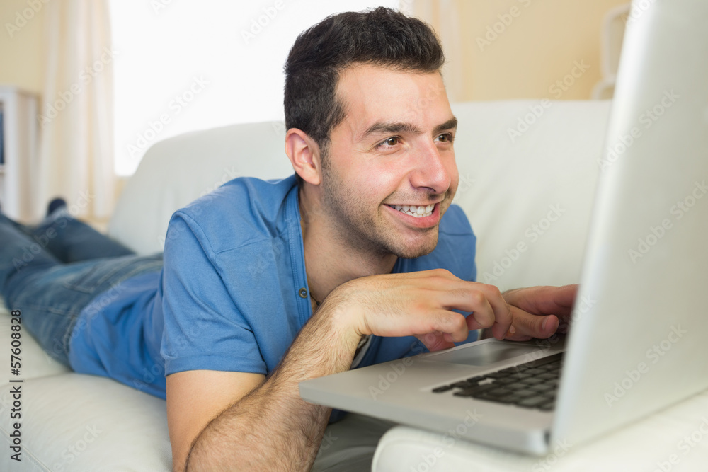 Casual cheerful man sitting on couch using and looking at laptop Casual cheerful man sitting on couch using and looking at laptop