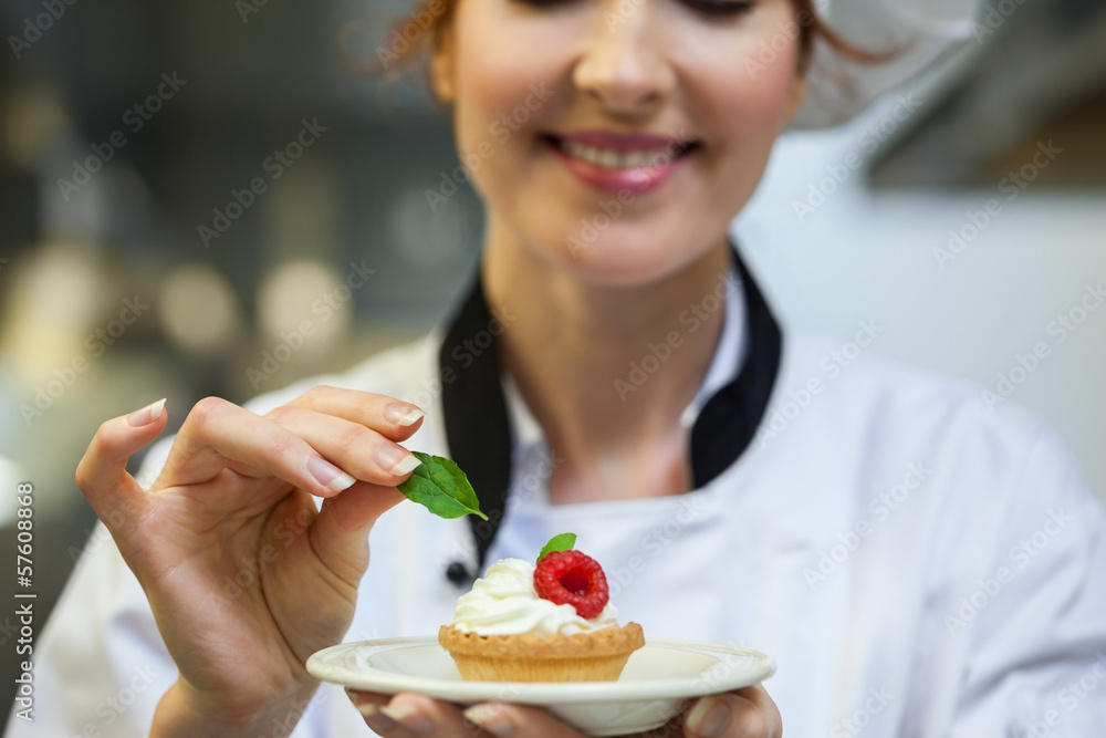 Smiling head chef putting mint leaf on little cake on plate Smiling head chef putting mint leaf on little cake on plate