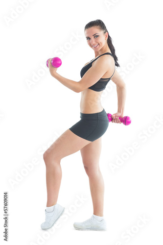 Side view of smiling active woman training with dumbbells