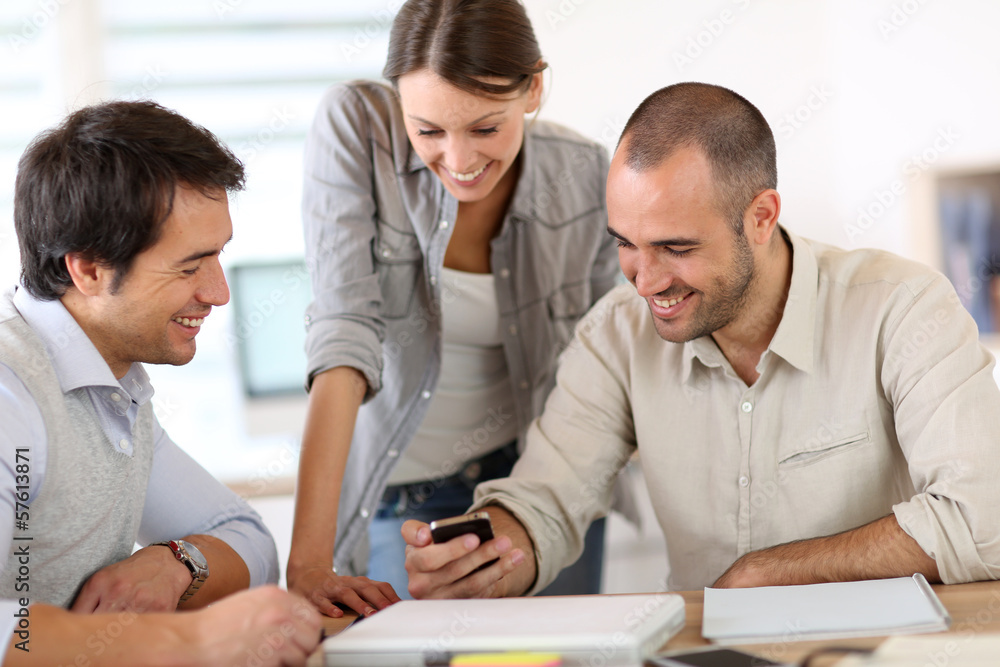 People in office laughing at reading text on smartphone People in office laughing at reading text on smartphone