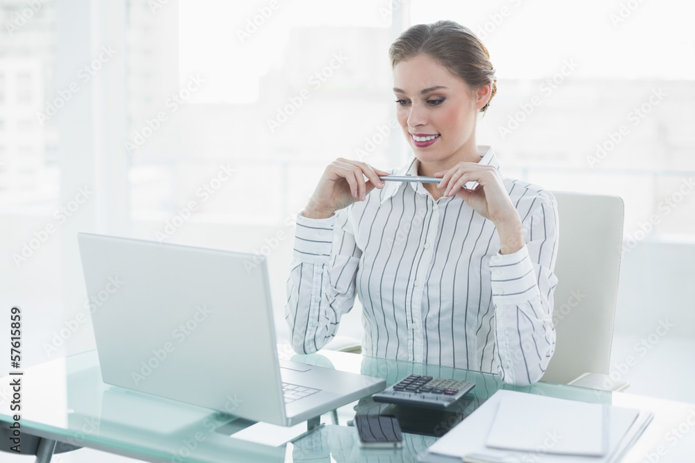 Attractive chic businesswoman holding a pencil sitting at her de Attractive chic businesswoman holding a pencil sitting at her de