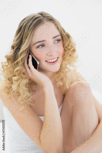 Pretty cheerful blonde sitting on bed phoning