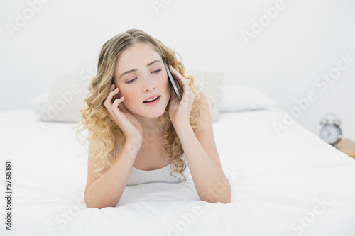 Pretty content blonde lying on bed phoning