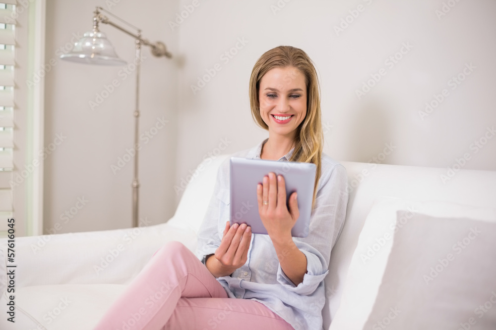 Smiling casual blonde sitting on couch using tablet Smiling casual blonde sitting on couch using tablet