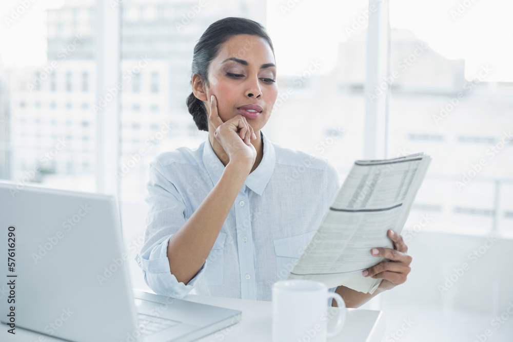 Focused businesswoman reading newspaper sitting at her desk Focused businesswoman reading newspaper sitting at her desk