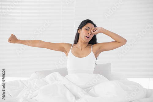 Lovely tired woman stretching out while sitting on her bed
