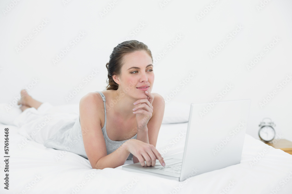 Thoughtful casual woman using laptop in bed Thoughtful casual woman using laptop in bed